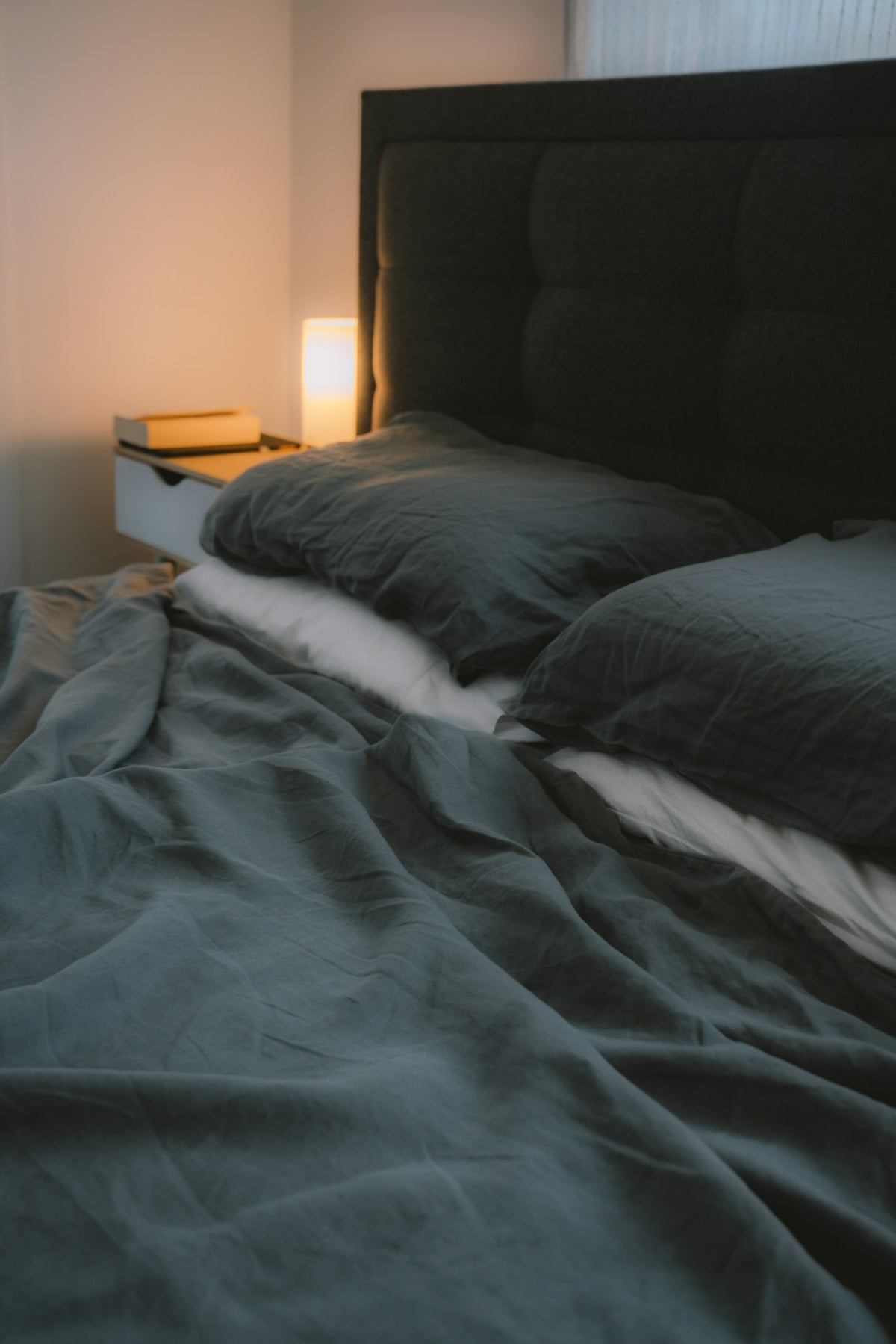 Dark bed linen beside wooden nightstand